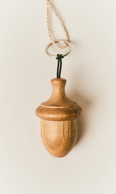 Plümo  The Acorn Keyring, crafted from solid oak and linseed-oil finished, hangs on a string against a white background.