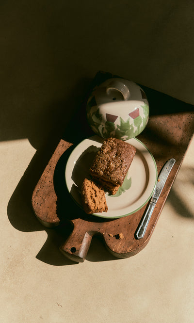 Plümo  A slice of bread and cookie on a plate beside the Thistle Cheese Dome, glowing in sunlight on a wooden board.