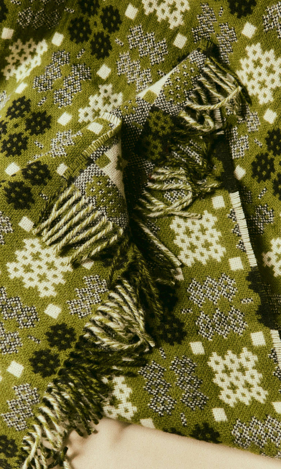 Plümo  Welsh Blanket - Apple Green: knit tapestry weave with geometric pattern and fringed edges, on beige surface.