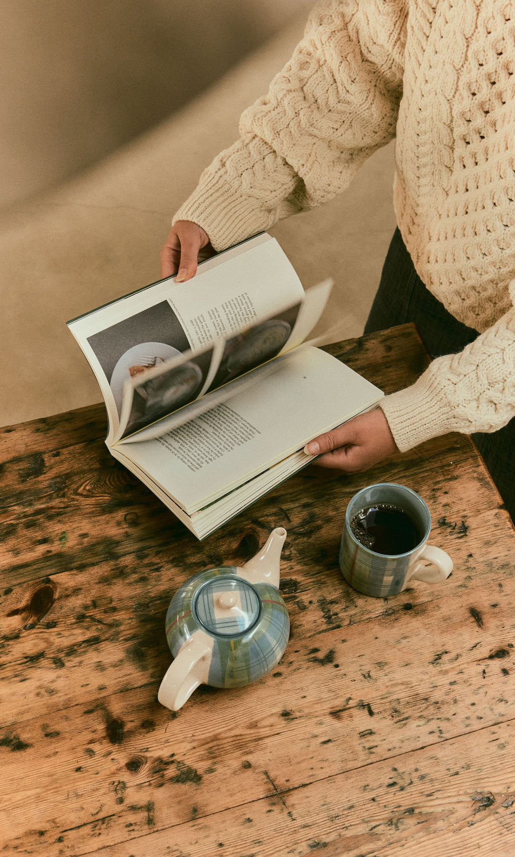 Plümo  Person in a cream sweater reads Vegetable Recipes by Jess Dennison at a rustic table with tea and teapot.