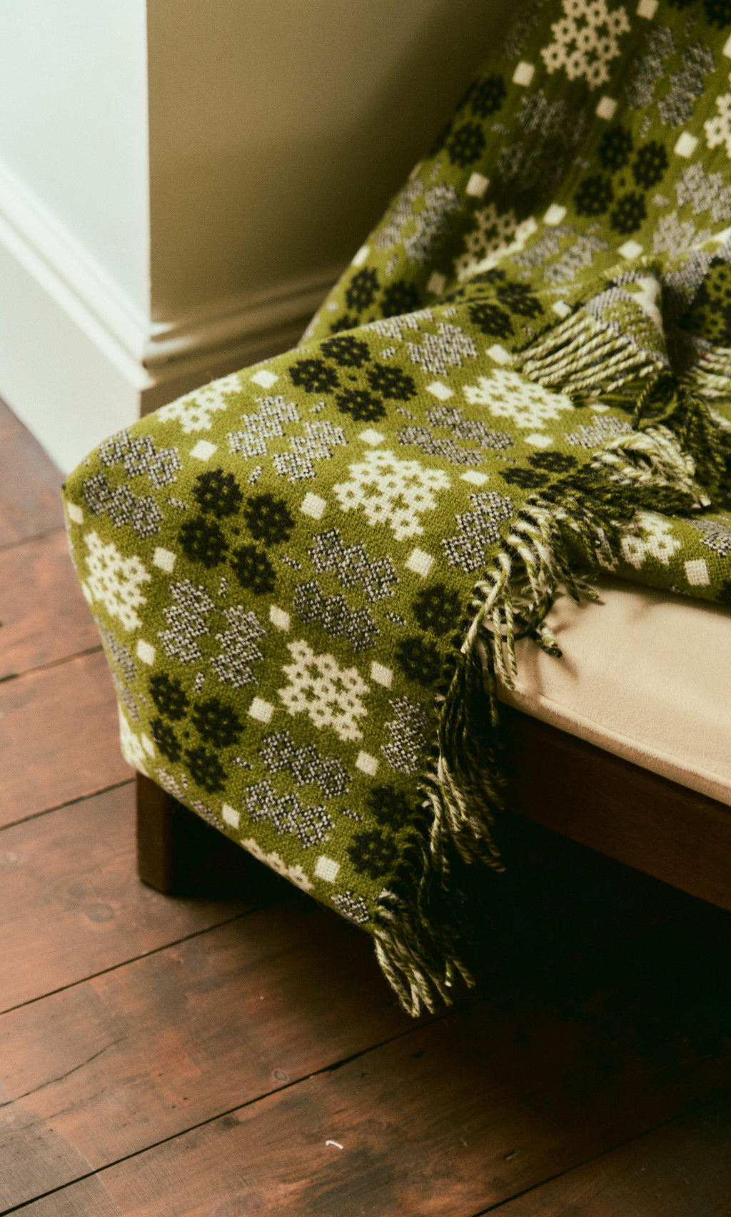 Plümo  Welsh Blanket - Apple Green with white and black patterns draped over a beige chair on a wooden floor.