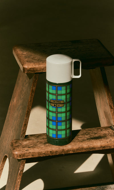 Plümo  Tartan Flask - Green with a white lid, resting on a wooden step stool.