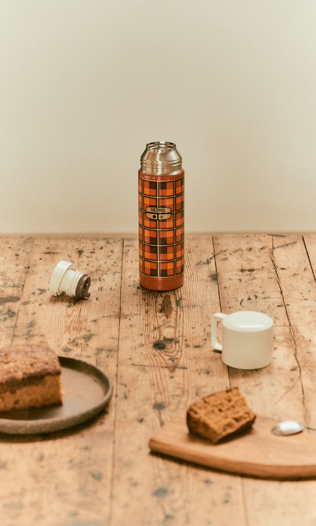Plümo  Tartan Flask - Orange on a wooden table with a piece of cake and a cup.