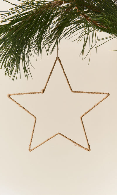 Plümo  A handmade Raffia Christmas Star made of twisted tan fiber hanging from a pine branch.