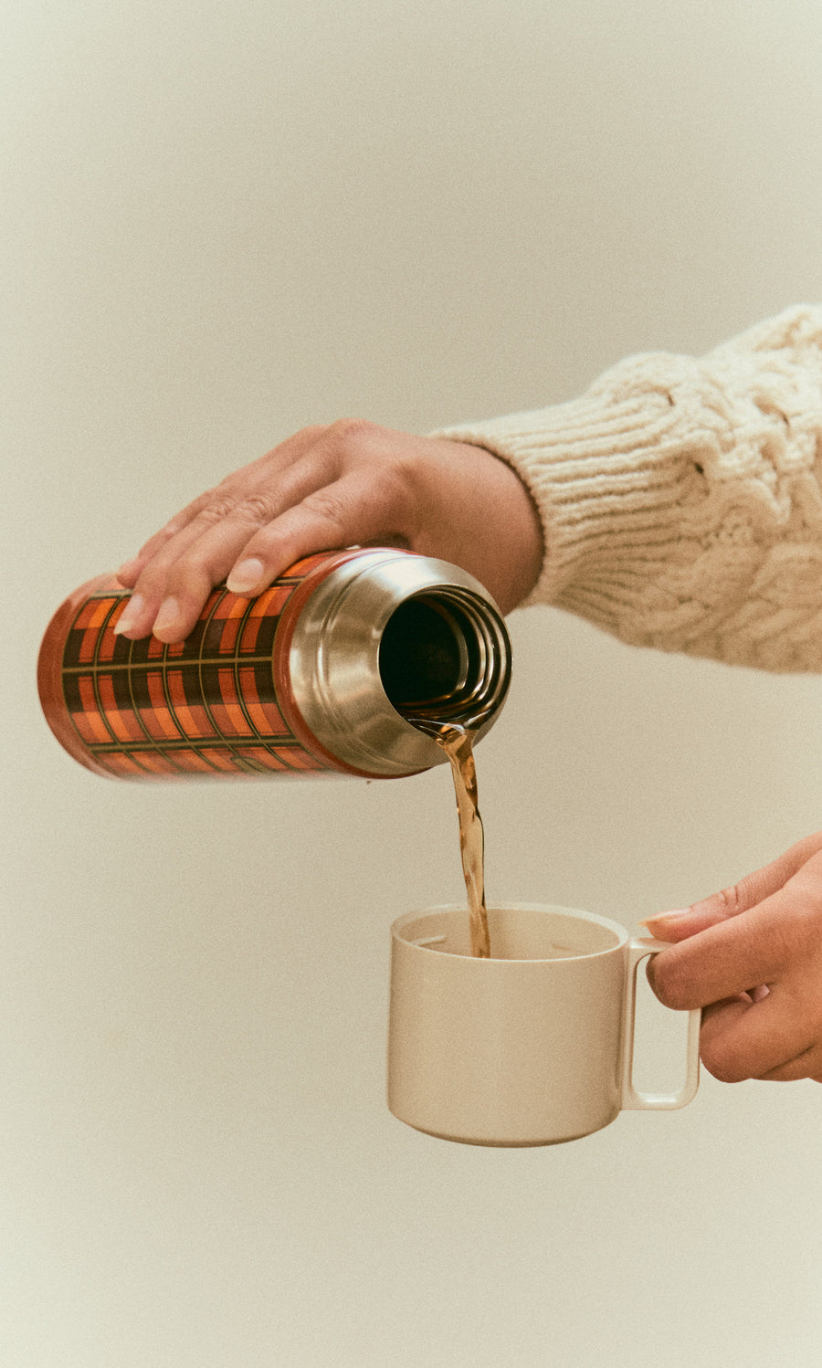 Plümo  A person pours coffee from an orange Tartan Flask - Orange stainless steel flask into a small cup.