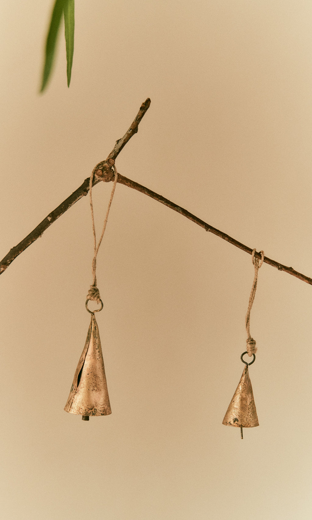 Plümo  Two Hanging Brass Bells - Small dangle from twine, chiming softly against a neutral beige background.