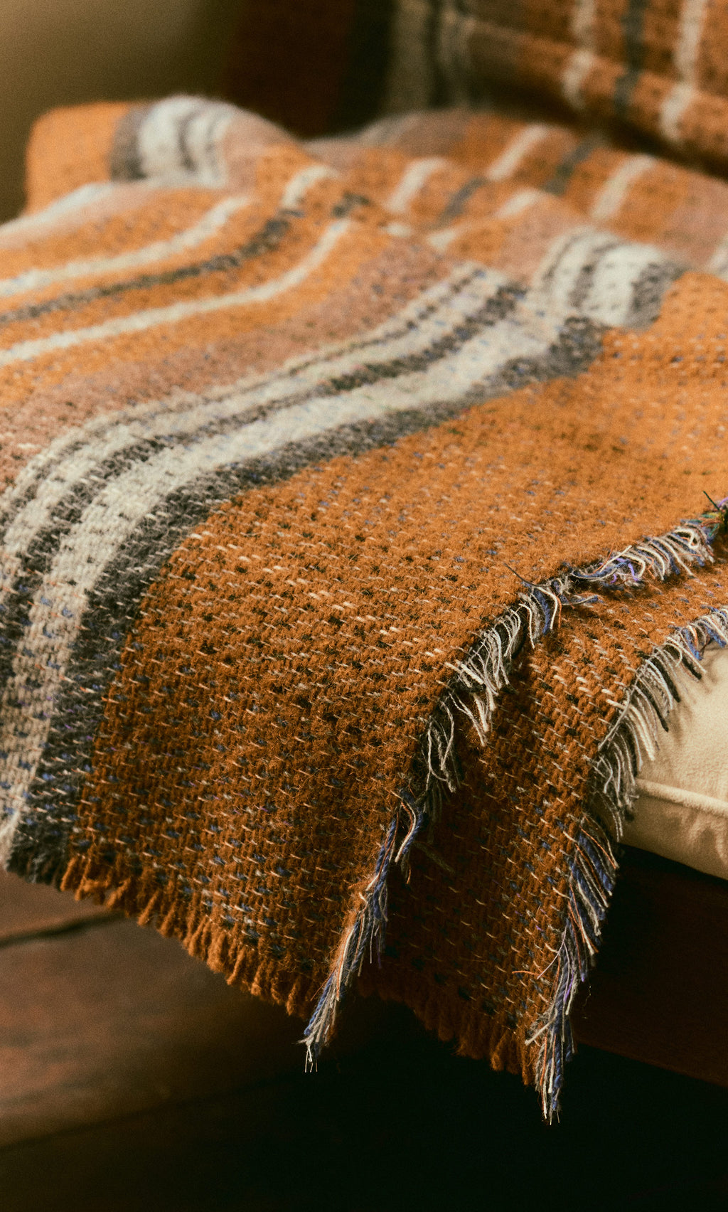 Plümo  A close-up of the Random Throw in brown and gray stripes draped over a padded chair.