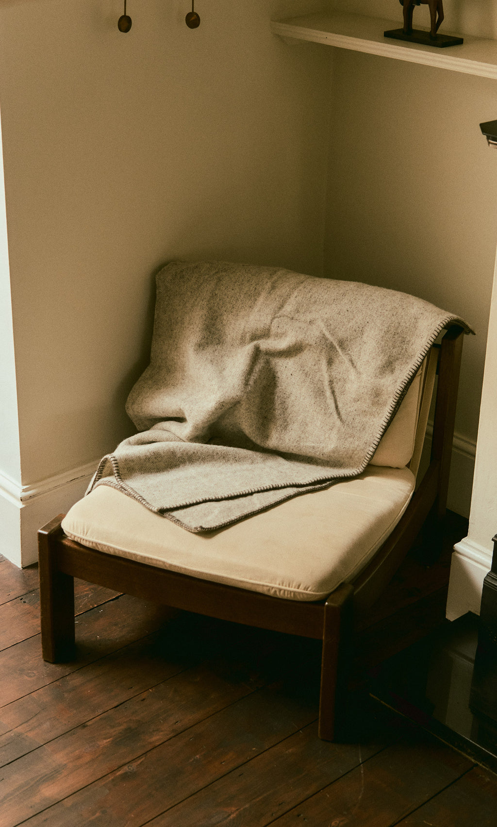 Plümo  A beige chair with the Kilkenny Blanket - Fossil draped over it sits on a wood floor in the corner.