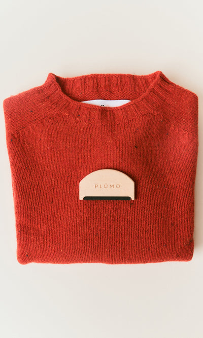 Plümo  A folded red sweater with a Wool Comb to remove pilling, set on a light background.