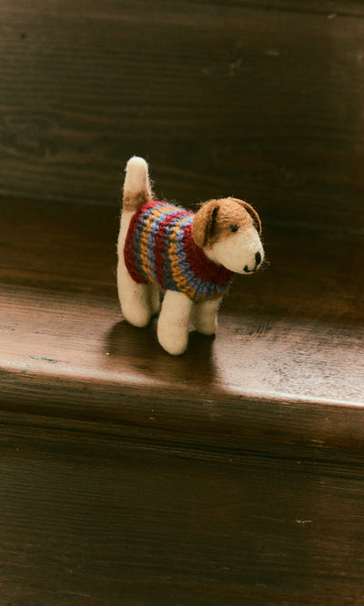 Plümo  Jack in a Jumper, a small plush dog in a colorful knit sweater, sits on a wooden staircase.