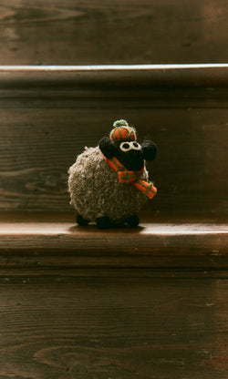 Plümo  Highland Sheep, a plush toy in scarf and hat, handcrafted in Nepal, sits on a wooden stair step.