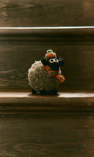 Plümo  Highland Sheep, a plush toy in scarf and hat, handcrafted in Nepal, sits on a wooden stair step.