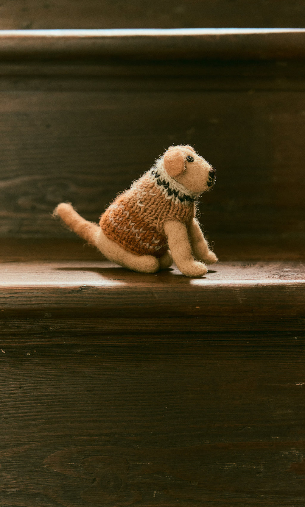 Plümo  Digby the Labrador, a small fairtrade Nepal wool plush, sits on a dark wooden stair step.