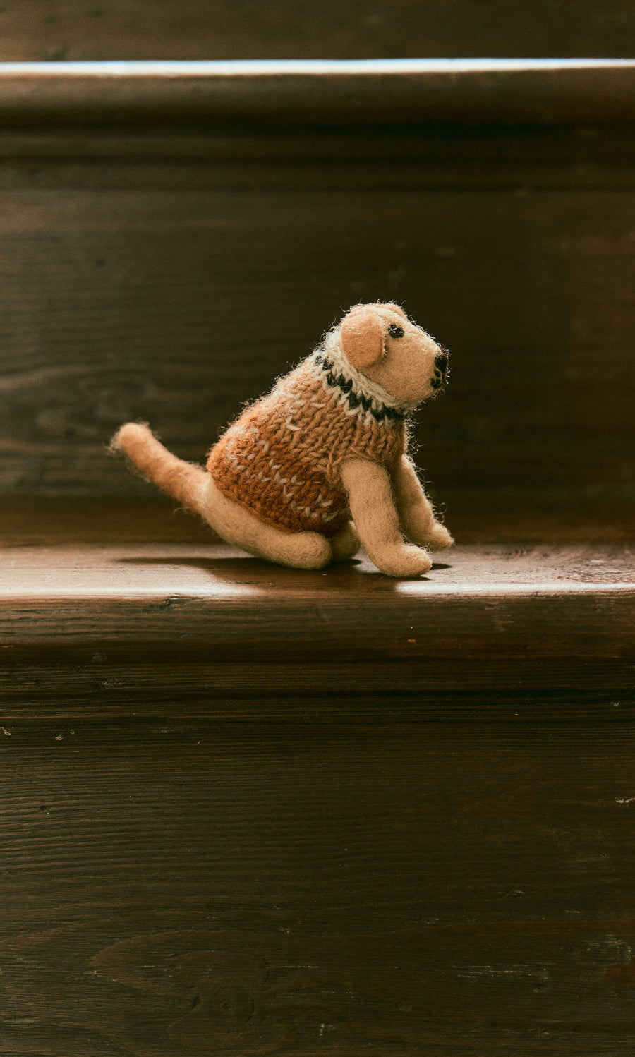 Plümo  Digby the Labrador, a small fairtrade Nepal wool plush, sits on a dark wooden stair step.