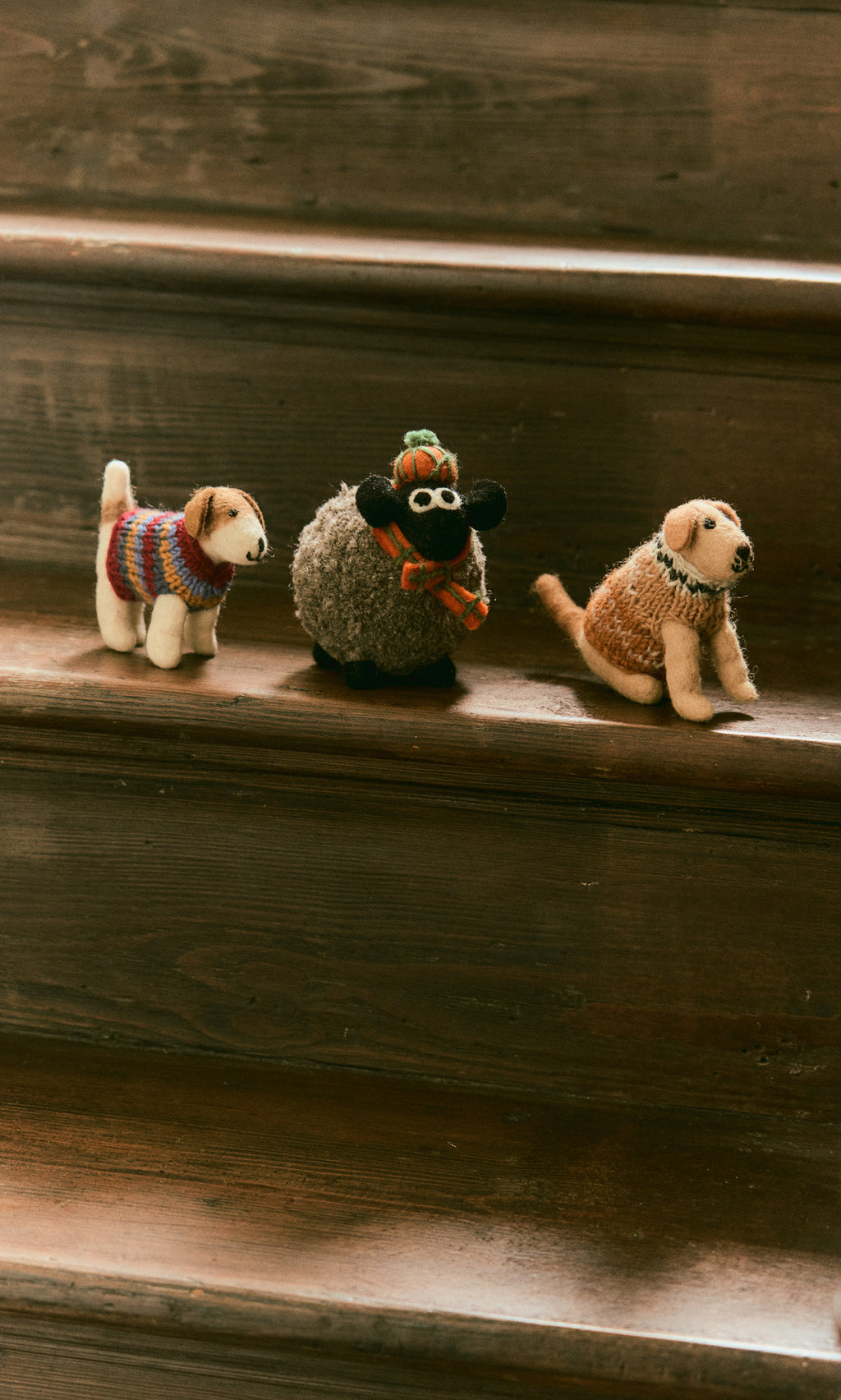 Plümo  Jack in a Jumper, a cozy woolly dog in a knit sweater, sits on wooden stairs with two other stuffed animals.