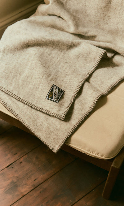 Plümo  Kilkenny Blanket - Fossil in tan pure new wool with whipstitched edges draped over a chair.