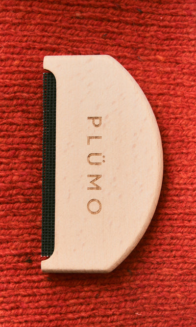 Plümo  The Wool Comb with PLÜMO engraving rests on a textured red fabric background.