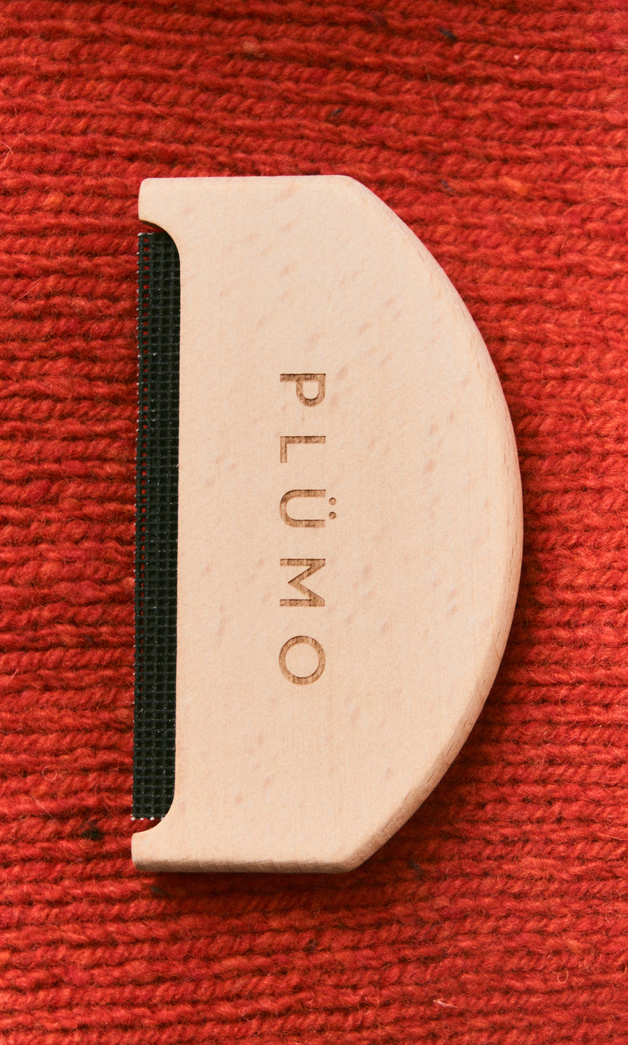 Plümo  The Wool Comb with PLÜMO engraving rests on a textured red fabric background.