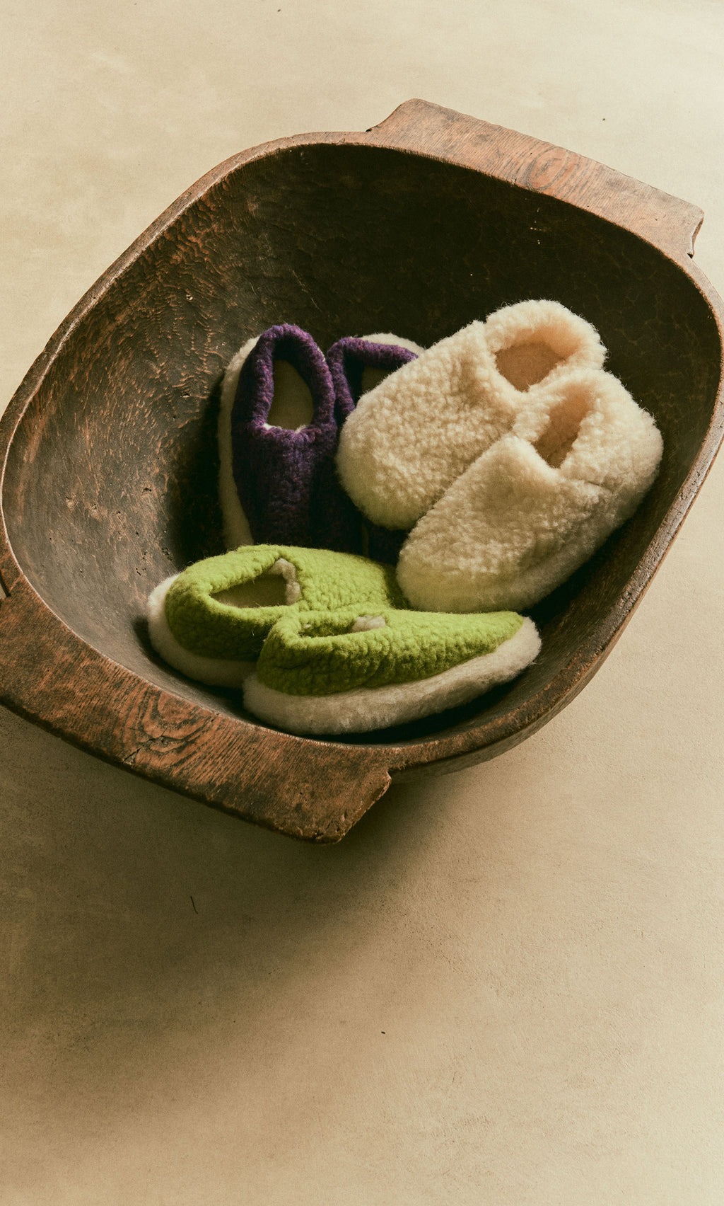 Plümo  A pair of Wool Slippers - Plum sits in an old wooden bowl on a beige surface.