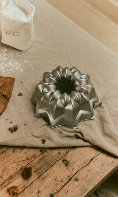 Plümo  Silver Star Cake Form, a star-shaped cast aluminium Bundt pan on a wooden table with a cloth.