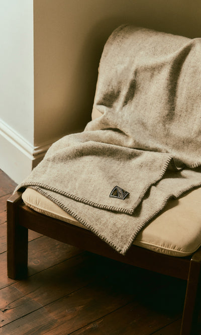 Plümo  A light grey Kilkenny Blanket - Fossil made of pure new wool draped over an armchair.