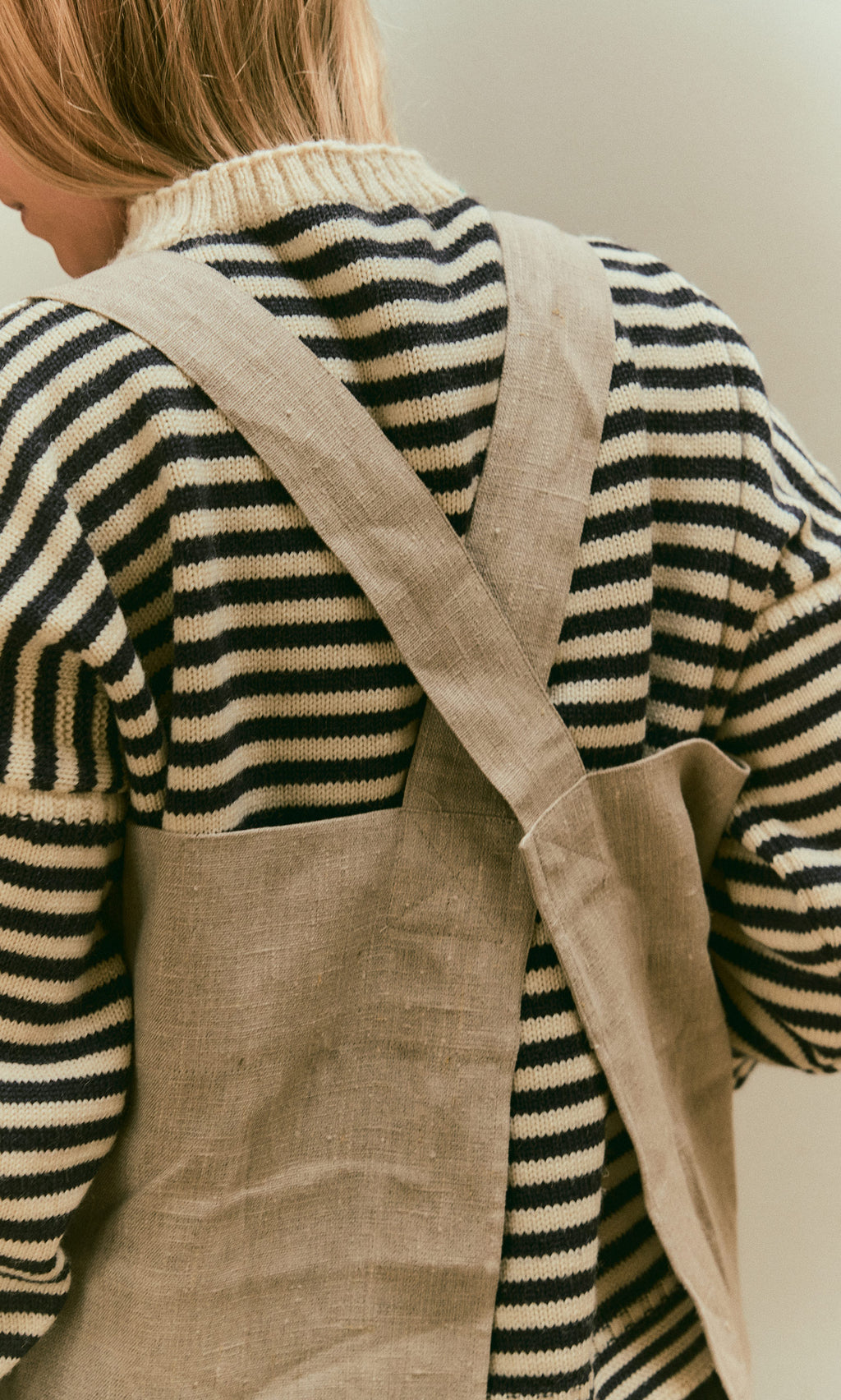 Plümo  Person in striped sweater wears Linen Pinafore Apron with deep front pocket, shown from behind.