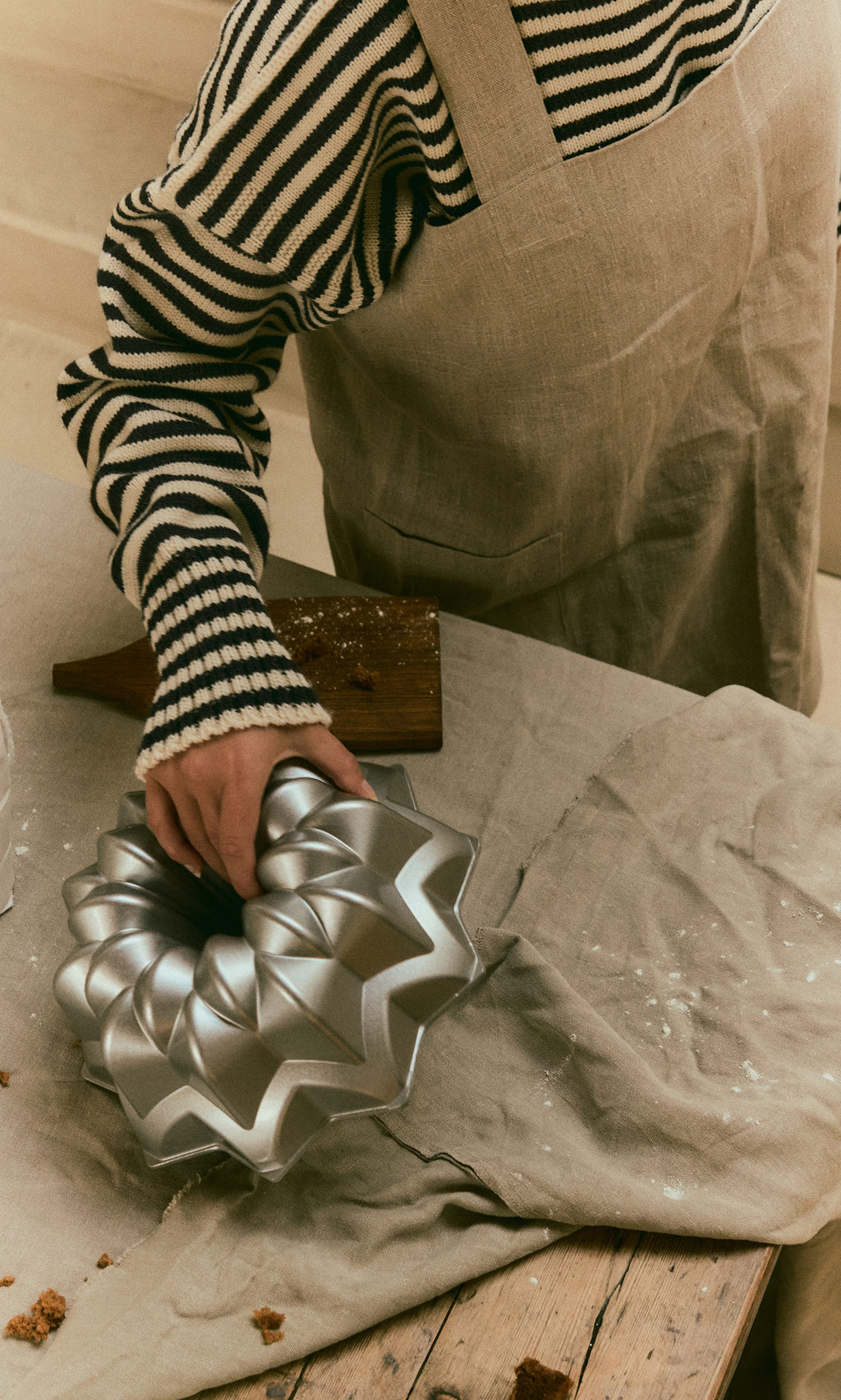 Plümo  A person in a striped sweater and apron places a Silver Star Cake Form on a floured wooden table.