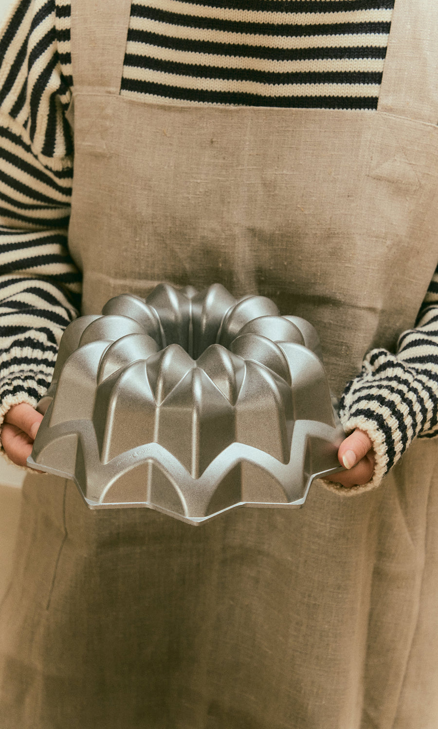 Plümo  A person in an apron holding a silver, star-shaped Silver Star Cake Form cast aluminium bundt pan.
