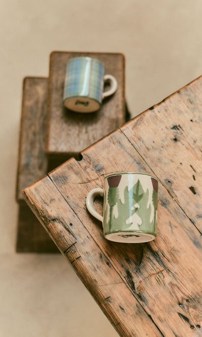 Plümo  A Thistle Mug on a rustic table, with another stacked on boxes in a cozy background.