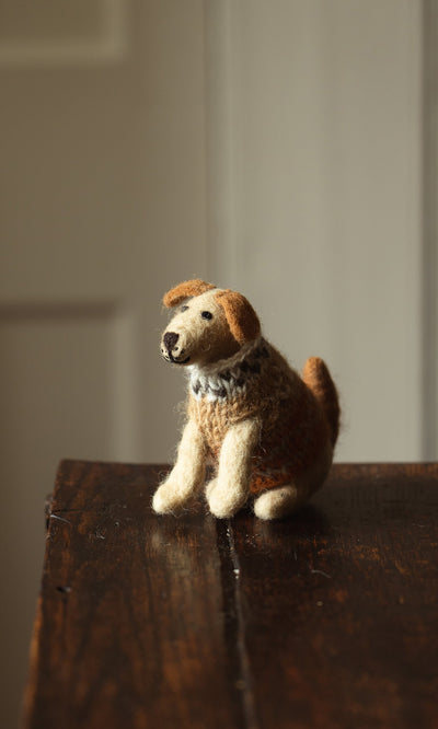 Plümo- Digby the Labrador, a small brown and white wool dog figurine, sits on a dark wooden surface in soft light.