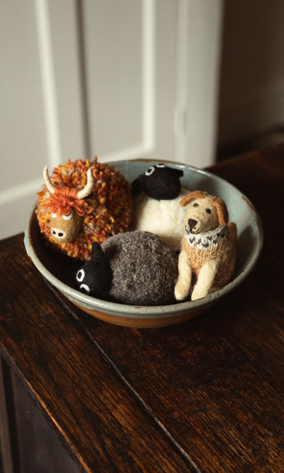 Plümo- A ceramic bowl holds fairtrade, hand-felted wool animals: Digby the Labrador, two sheep, and an orange cow with horns.