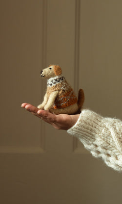 Plümo- A hand in a knitted sleeve holds Digby the Labrador, a handcrafted dog figurine, against a plain background.