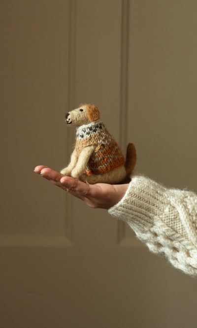 Plümo- A hand in a knitted sleeve holds Digby the Labrador, a handcrafted dog figurine, against a plain background.