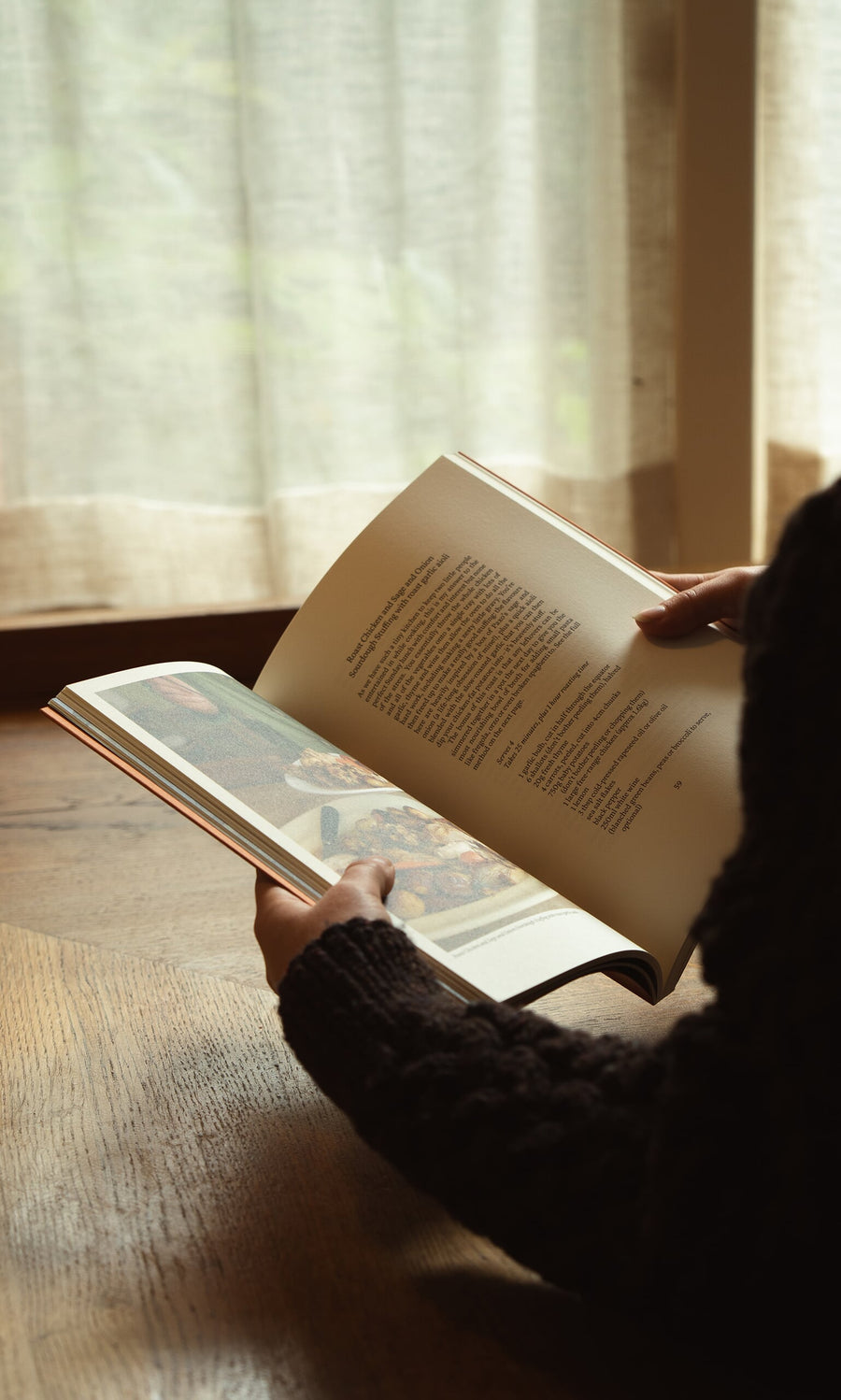 Plümo- Someone reads Weekend Recipes by Jess Elliott Dennison by a window with sheer curtains, sunlight streaming in.