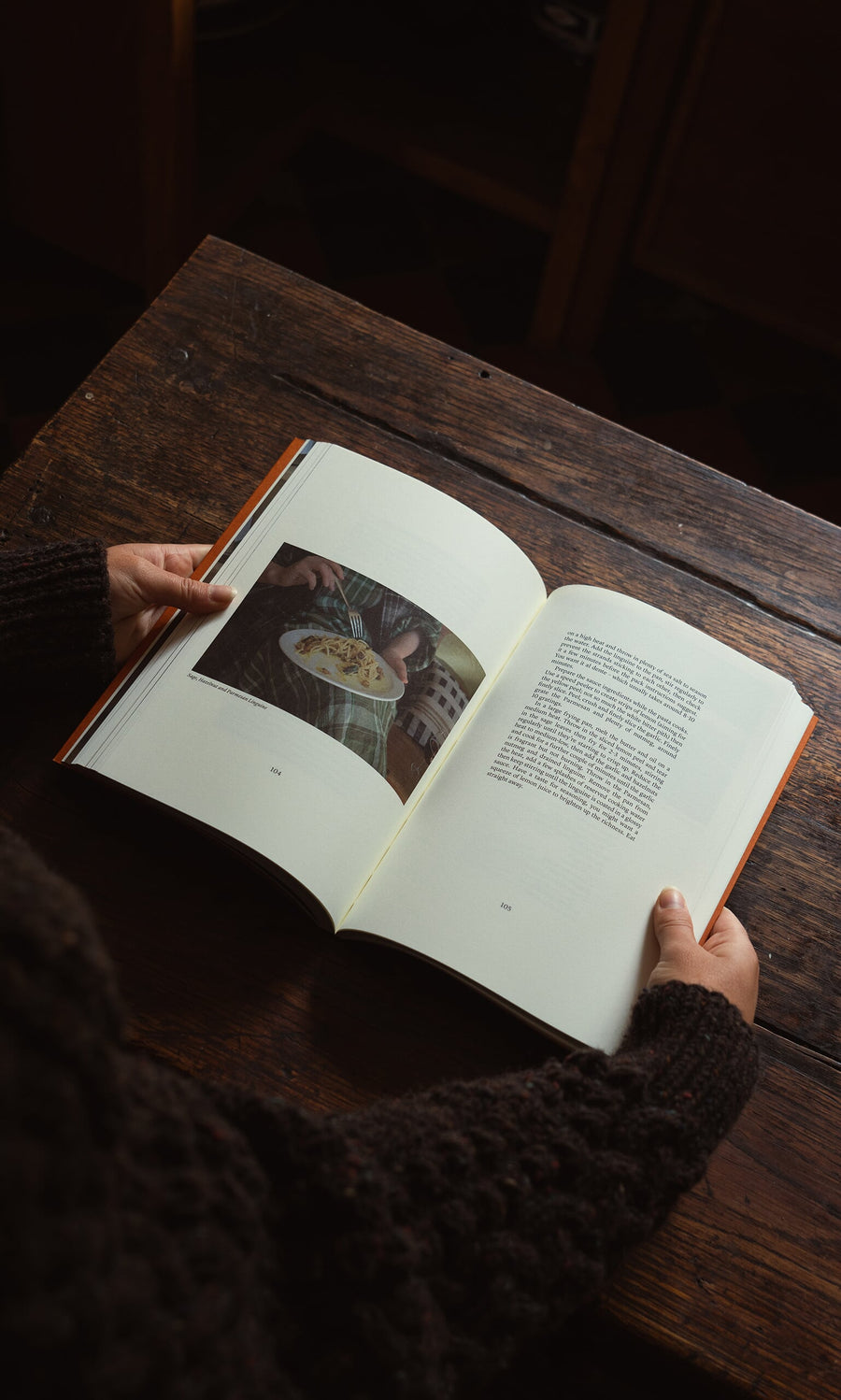 Plümo- Person holding "Weekend Recipes by Jess Elliott Dennison" open on a wooden table.