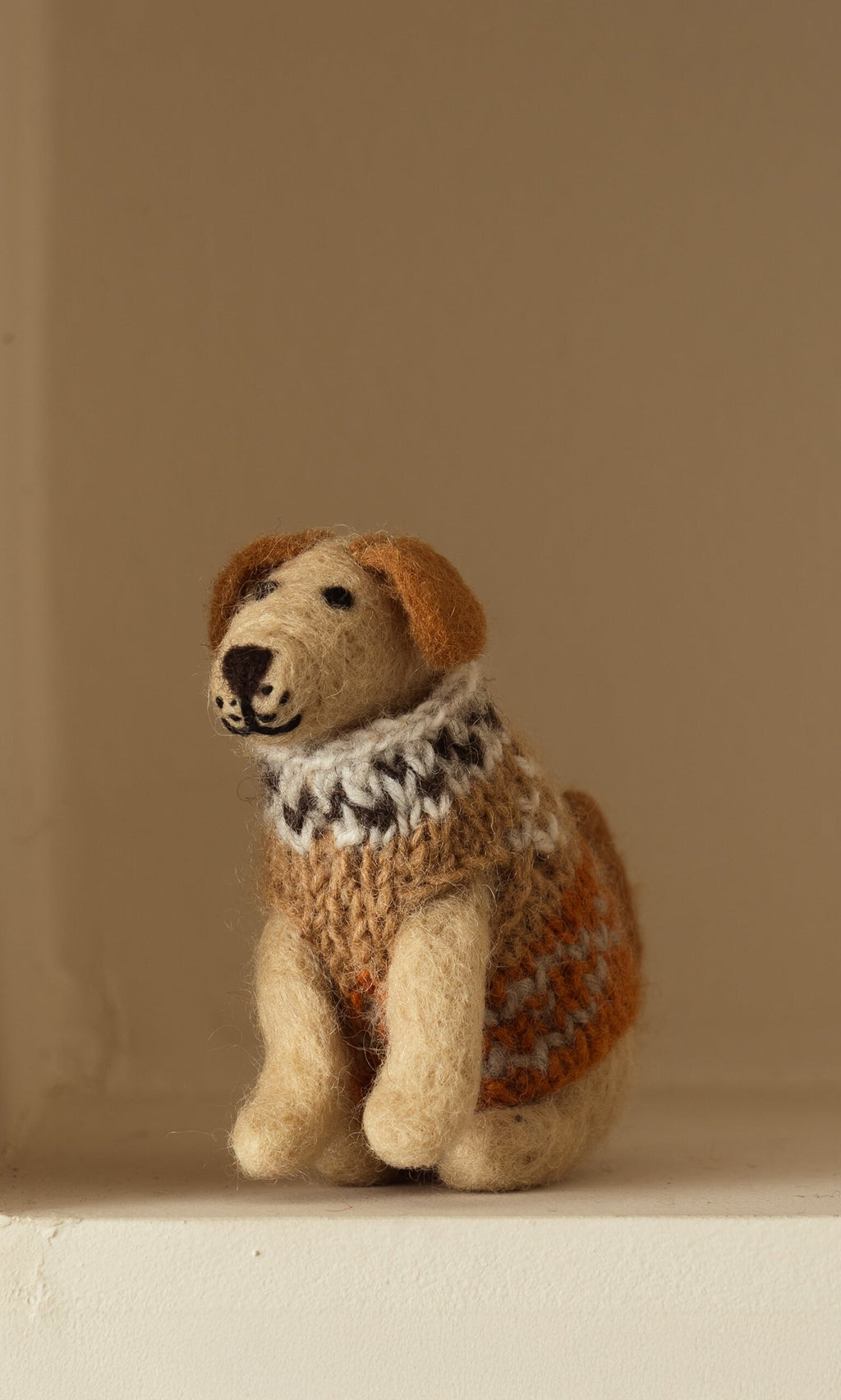 Plümo- Digby the Labrador, a small hand-felted wool dog in an orange, white, and brown sweater, sits on a light surface.
