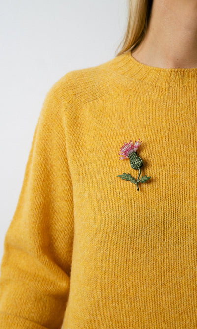 Plümo- Person wearing a Thistle Brooch—an embroidered pink thistle, perfect as a gardening gift.