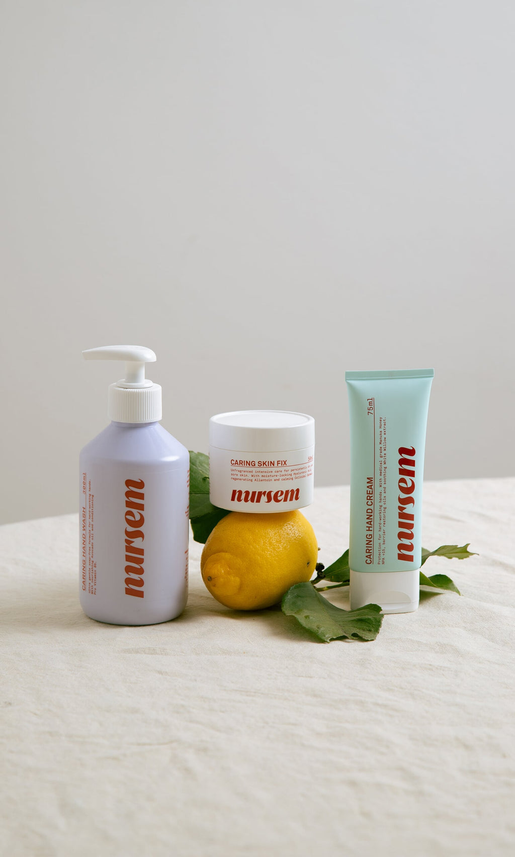 Plümo- Nursem Hand Cream (75ml) with Manuka honey arranged on a cloth beside a lemon and green leaves.