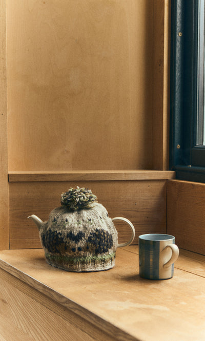 Plümo  A Blue Tartan Mug sits with a teapot in a cozy on a wooden windowsill lit by natural light.