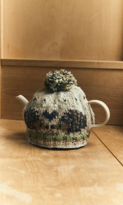 Plümo  A white teapot with a Hedgehog Tea Cosy and pom-pom sits on a wooden surface.