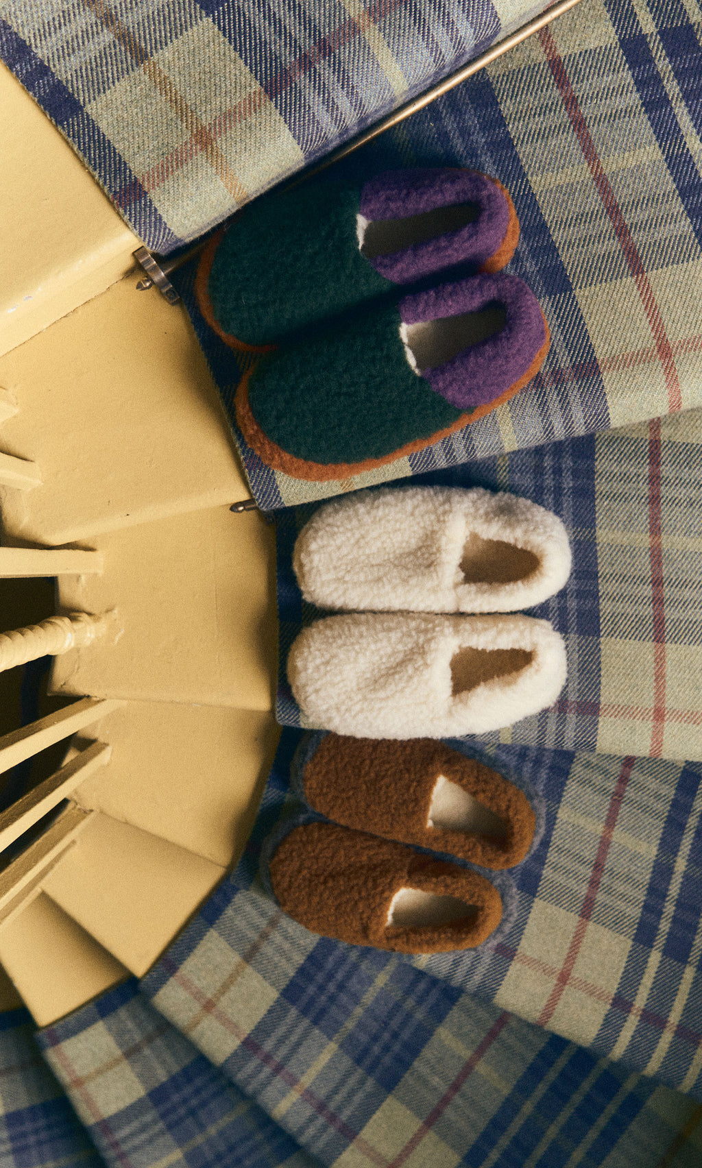 Plümo  A pair of Wool Slippers - Caramel rests on plaid fabric beside yellow stairs.