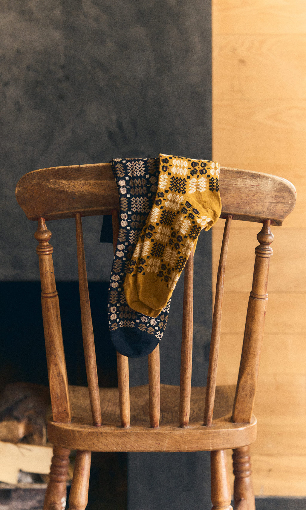 Plümo  Two patterned socks, including Welsh Socks - Gold, draped over a wooden chair indoors.