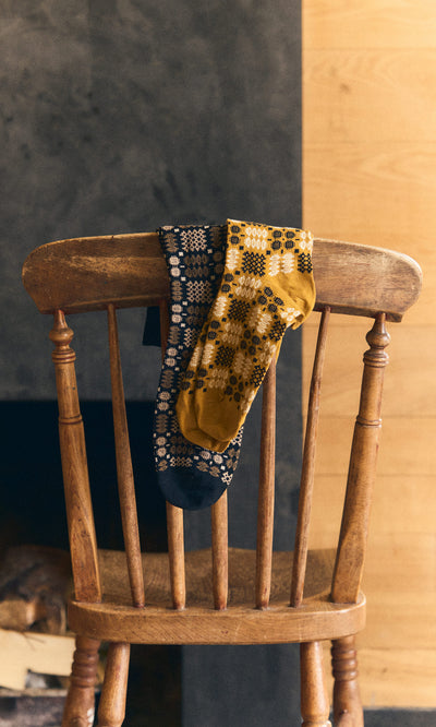 Plümo  Two patterned socks, including Welsh Socks - Gold, draped over a wooden chair indoors.