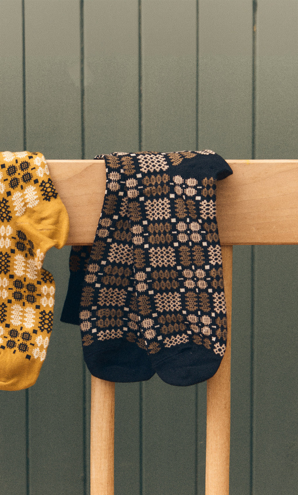 Plümo  Welsh Socks - Soot in black and brown on a wooden chair, with a yellow sock peeking out on the left.