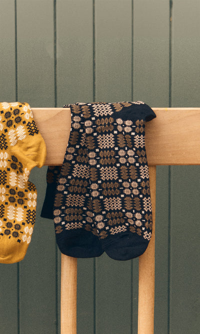 Plümo  Welsh Socks - Soot in black and brown on a wooden chair, with a yellow sock peeking out on the left.
