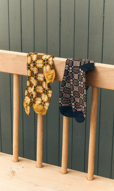 Plümo  Two Welsh Socks - Soot hang over a wooden railing, set against a green paneled wall.