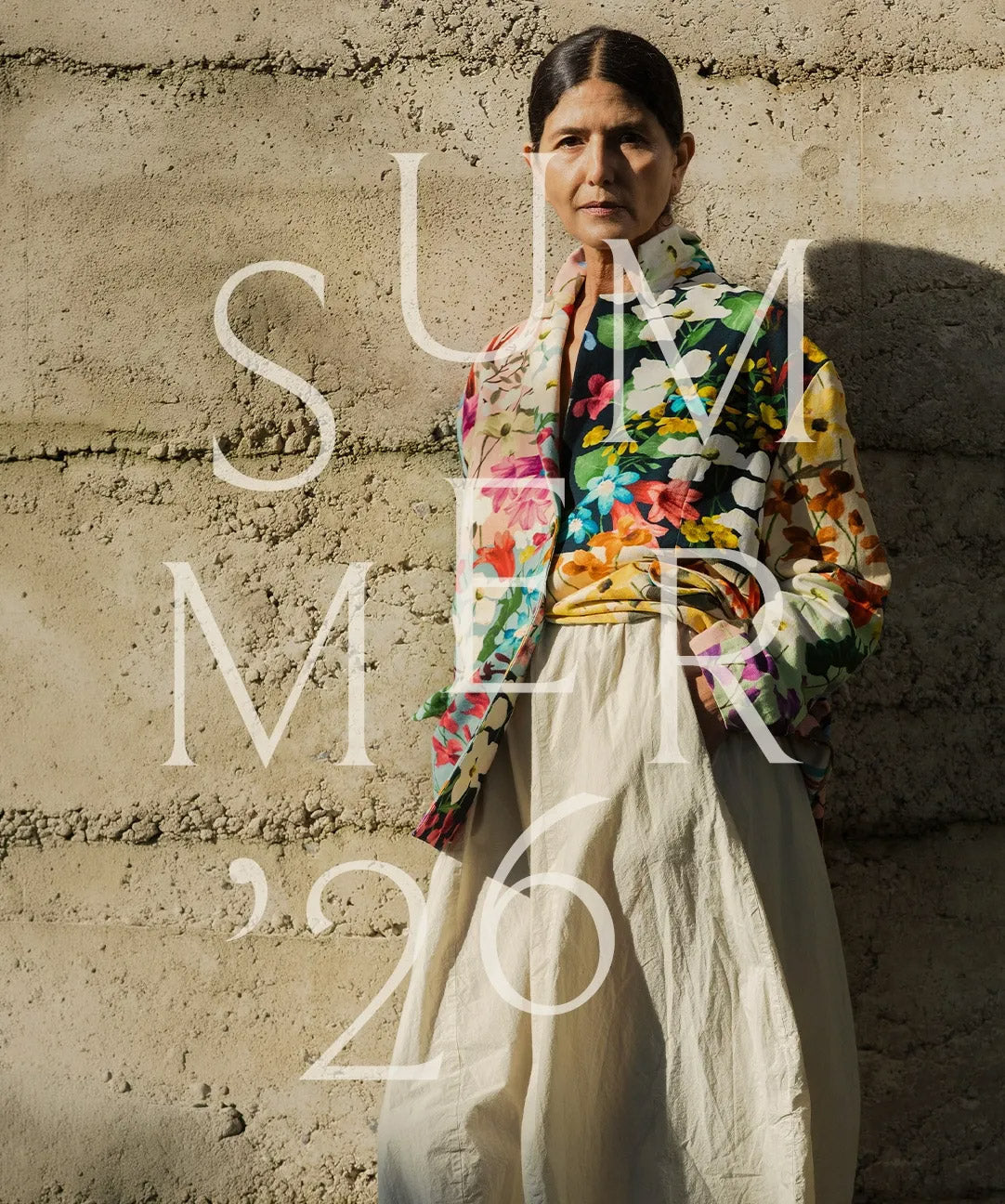 Person wearing a colorful floral shirt and white pants against a textured wall with 'Summer '26' text overlay.