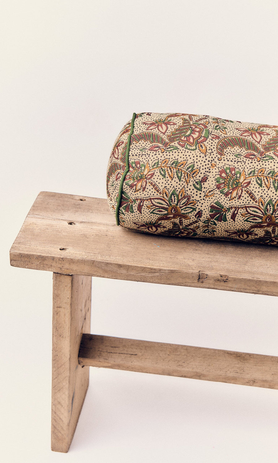 Plümo- A Printed Bolster Cushion with floral vines sits on a wooden bench against a plain background.