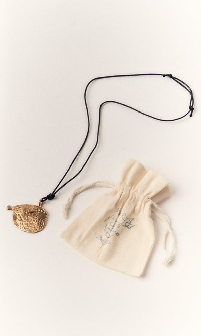 Plümo- The Puffer Fish Necklace features a handcrafted bronze puffer fish pendant on a black cord, shown with a cream pouch.