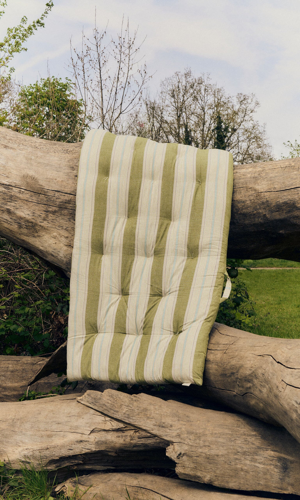 Plümo- A Quilted Mattress - Green Stripe, sustainable, draped over large fallen tree trunks outdoors.